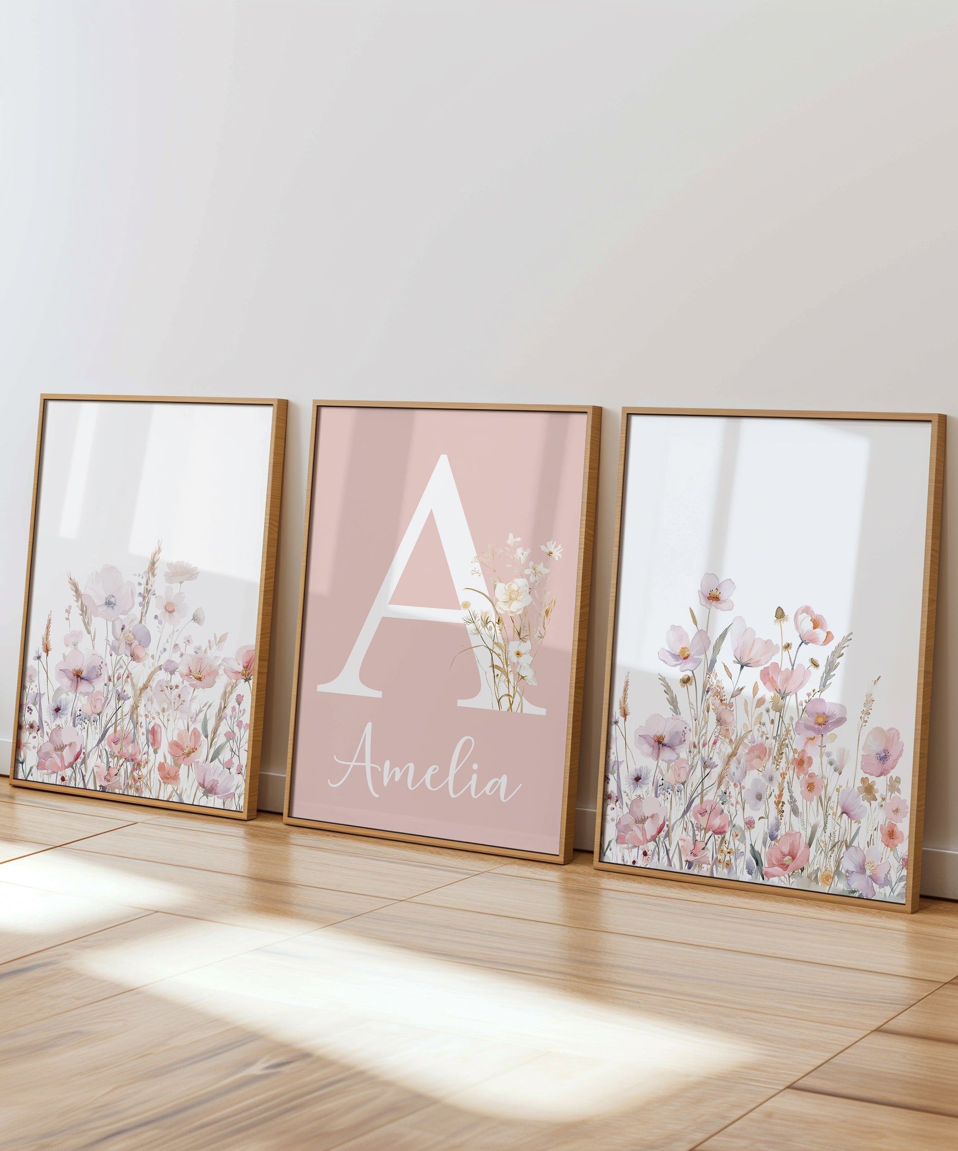 A set of 3 girls nursery prints featuring the two end prints with beautiful light pink and purple wildflowers and the centre nursery print with your child's name written in a cute font with the first initial written in a large serf font above and set on a light pink background.