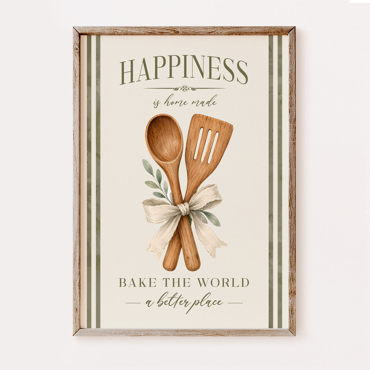 A framed kitchen wall art print with a rustic wood frame, featuring the words “HAPPINESS is home made” and “BAKE THE WORLD a better place,” with two wooden utensils tied with a cream ribbon and small green leaves on an off-white background.