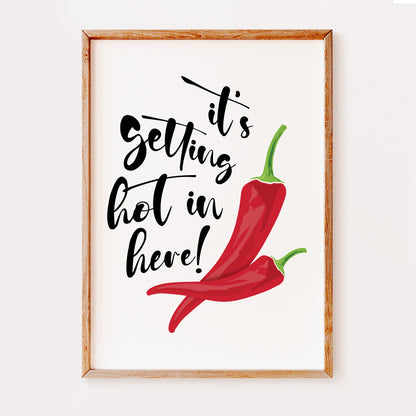 A kitchen art print illustrating two red chili peppers and displaying the quote 'It's getting hot in here' in a fun and stylish black font set on a white background.