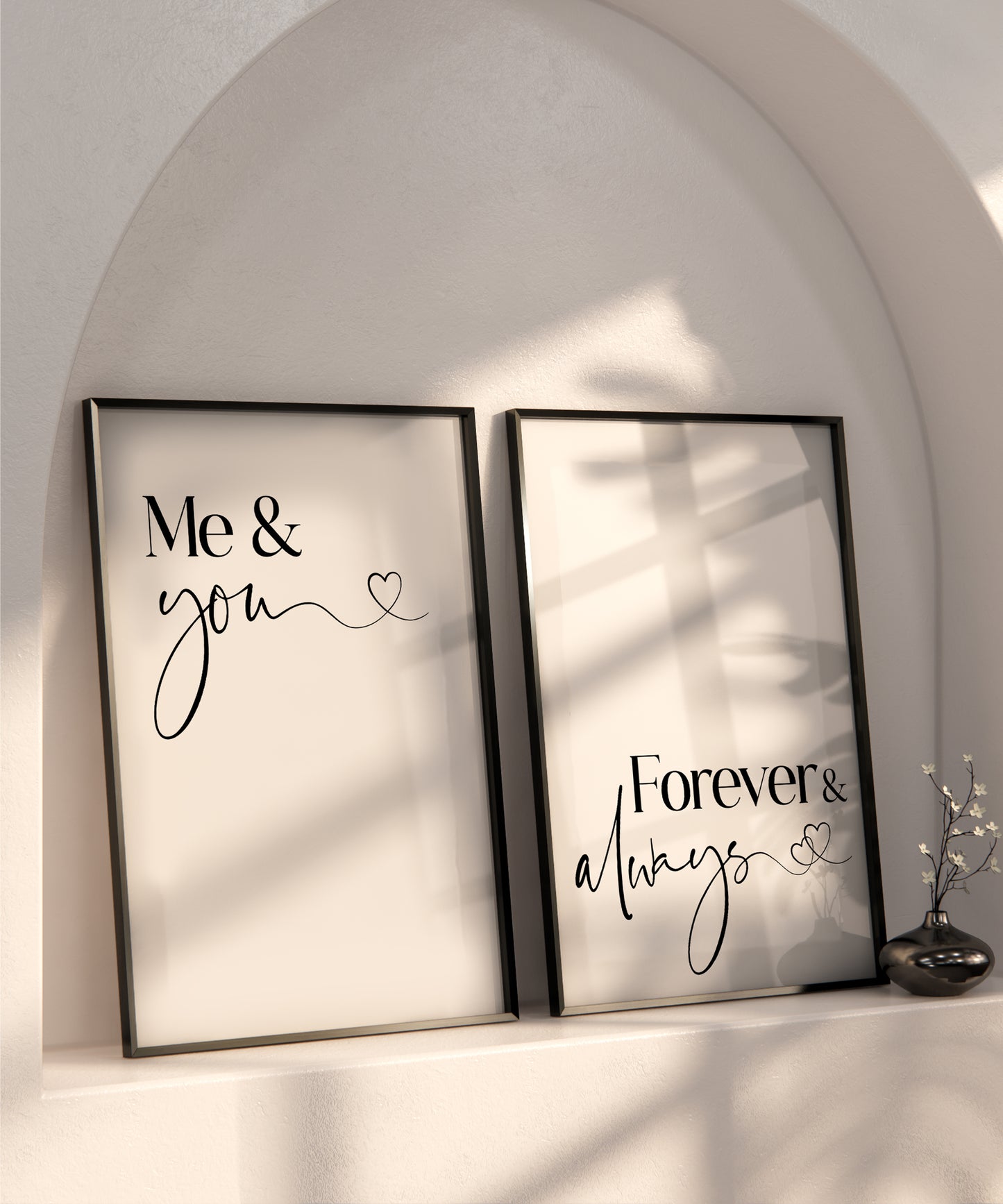 A set of 2 bedroom prints displayed in black frames on a recessed shelf in a wall. The prints read 'Me & You' and 'Forever & Always' written in a sophisticated black font set on a white back ground.
The last letters of 'you' and 'always' have a wavy tail that leads to a little love heart on the end.