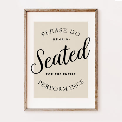 Funny minimalist bathroom wall art print with “Please Remain Seated for the Entire Performance” quote in black typography on a neutral beige background in a wooden frame.